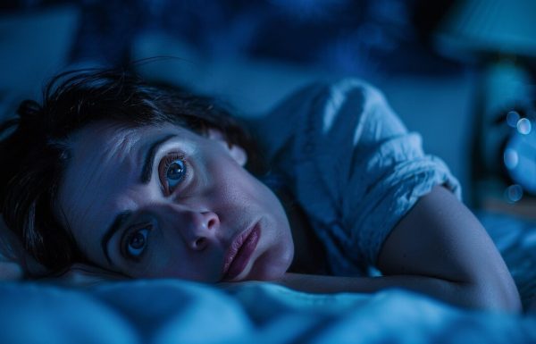 Professional woman lying awake at night unable to sleep before a big presentation with alarm clock visible