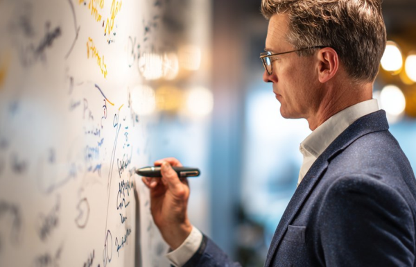 Professional presenting pilot programme results at a whiteboard in a modern office, navy blazer, warm lighting, engaged and confident